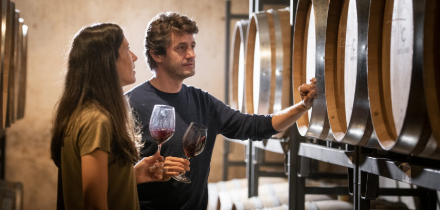 Zwei Personen verkosten Wein vor Fässern im Weinkeller.